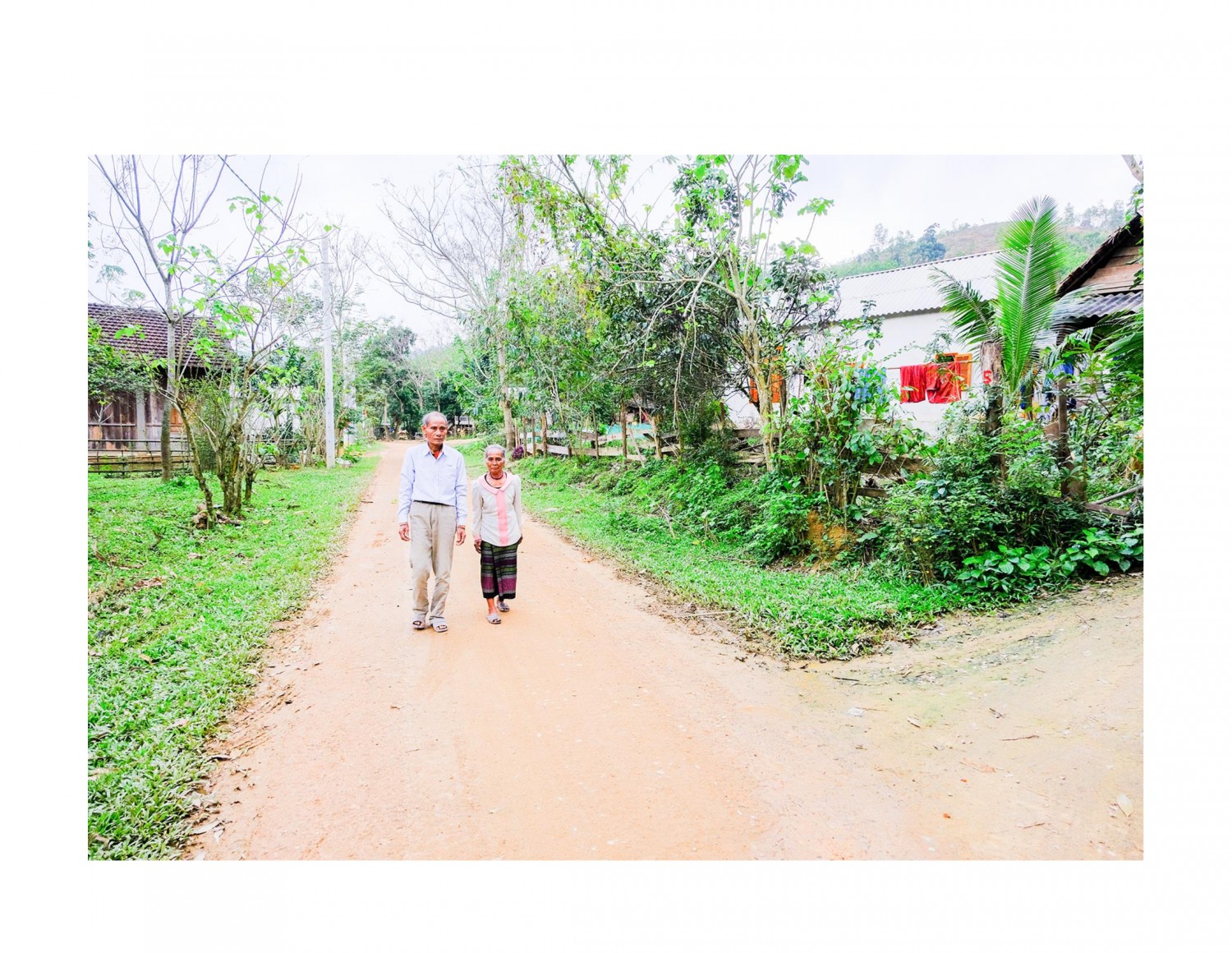 Vợ chồng ông Thủy đi trên con đường bê tông sạch đẹp, nơi trước đây là vườn cây ăn quả của gia đình